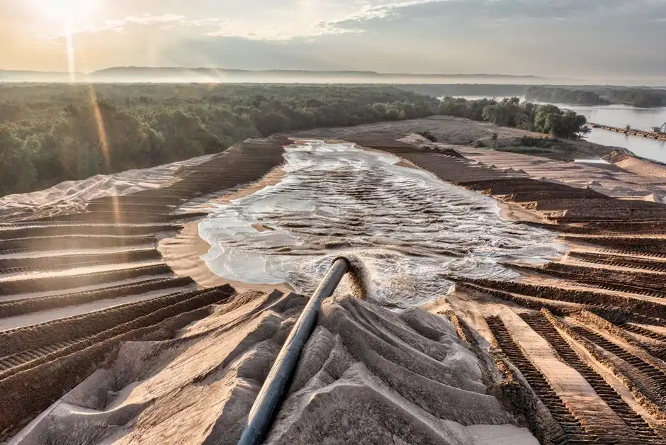 Drone shot of sand processing with flowing water and forest backdrop in Reads Landing, MN, at sunset.